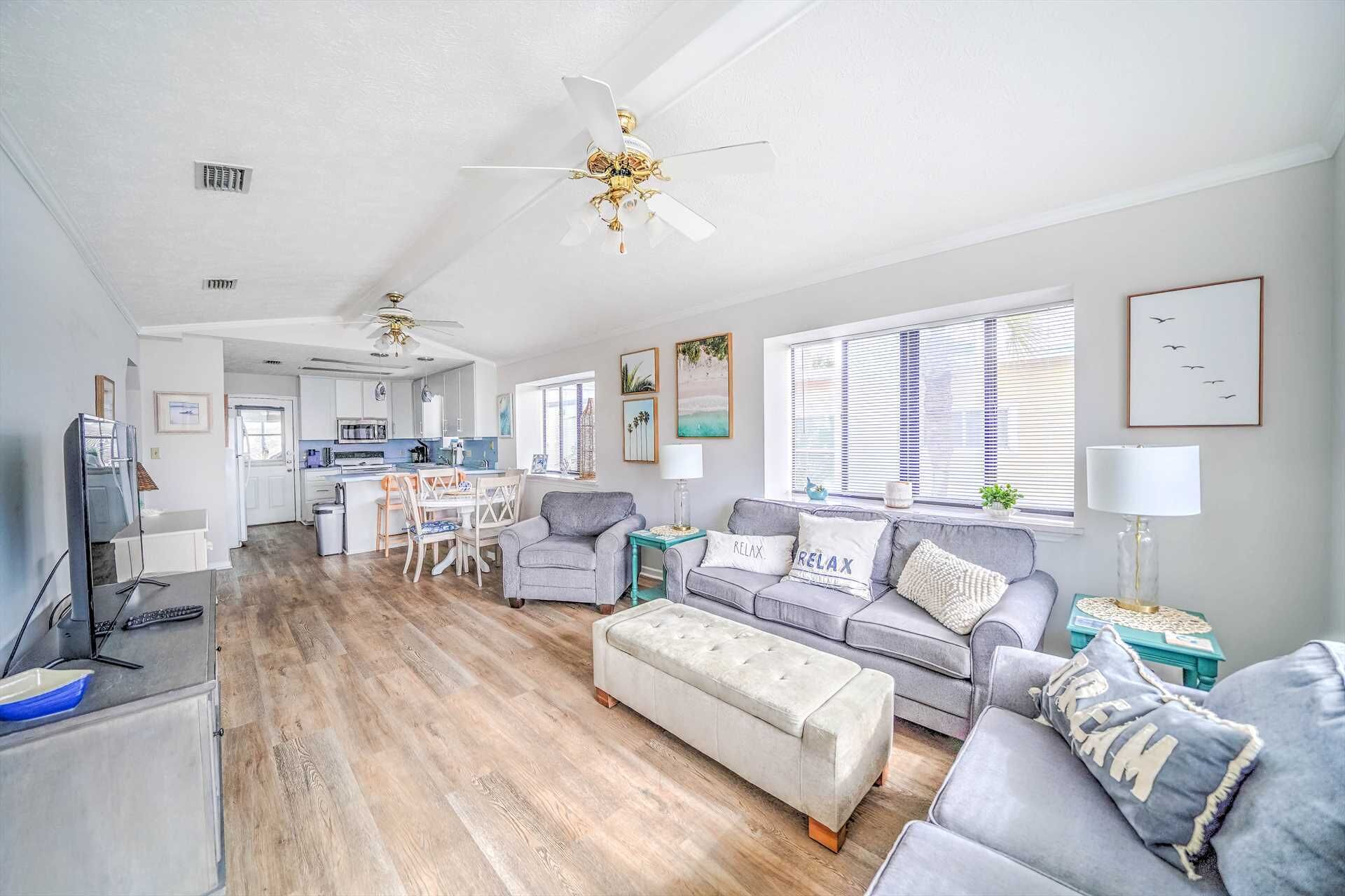 A modern living room with a grey sofa, a matching ottoman, and a ceiling fan.
