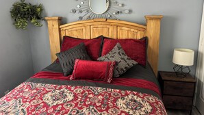Une chambre à coucher avec une tête de lit en bois, une couvre-lit à motifs et un miroir orné d’un motif en forme de soleil sur le mur.