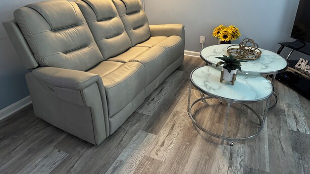 Un salon moderne avec un canapé en cuir gris, deux petites tables rondes en marbre et un téléviseur posé sur un meuble.