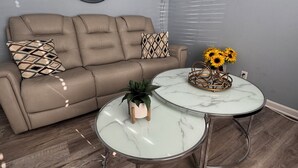 Un salon avec un canapé, deux tables rondes, une plante en pot et un tableau accroché au mur.