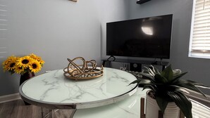 Un salon moderne avec une table en marbre, un téléviseur à écran plat, un tableau représentant Paris et une plante en pot.