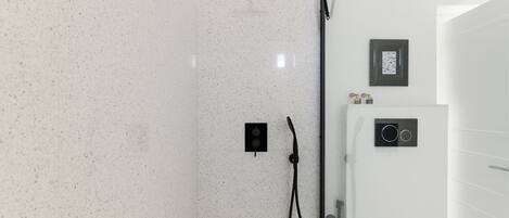 A modern bathroom with a white speckled tile wall, a black showerhead, and a wall-mounted control panel.