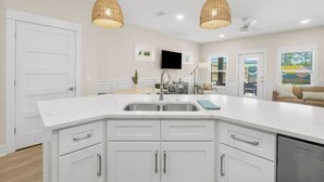 A modern kitchen with white cabinetry, a large island, and two wicker pendant lights. - Large Home~Short Walk to Beach+Saltwater Pool l Sleeps 24 (Panama City Beach)