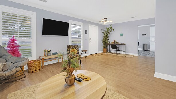 A spacious living room with a wooden floor, a round coffee table, a grey sofa, and a television mounted on the wall. - 2680- Space Cadet, Single Level, Big Yard, Large Living Area, Pet & Kid Friendly (Jacksonville)