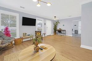 Un salon spacieux doté d’un parquet, d’une table basse ronde, d’un canapé gris et d’un téléviseur fixé au mur.