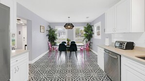 A modern kitchen with white cabinets, a black and white patterned floor, a dining area with two chairs, and a kitchen island with a toaster. - 2680- Space Cadet, Single Level, Big Yard, Large Living Area, Pet & Kid Friendly (Jacksonville)