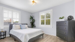 A bedroom with a bed, a dresser, a plant, and two windows with blinds. - 917- San Marco Sky Cottage, Pets OK, Near Arenas & Hospitals (Jacksonville)
