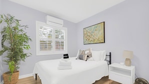 Une chambre à coucher avec un lit, une table de chevet, une lampe et une plante en pot.