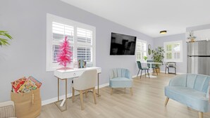Un salon moderne avec un bureau blanc, deux chaises, un canapé et un téléviseur.