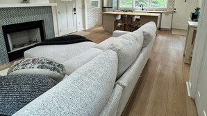 Een ruime woonkamer met een grote zithoek, een open haard en een keukenhoek met een eettafel en stoelen.