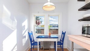 A dining area with a white table, blue chairs, a pink rug, and a window with a view of trees and a building. - Modern Loft in Historic Birdtown - Unit 8 (Lakewood)