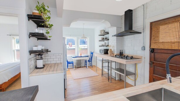 A modern kitchen with a central island, a dining area with blue chairs, and a view of the outdoors. - Modern Loft in Historic Birdtown - Unit 8 (Lakewood)