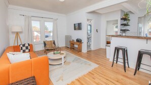 A spacious living room with a sofa, coffee table, and a small desk. There is a kitchen area with a bar and stools. - Modern Loft in Historic Birdtown - Unit 8 (Lakewood)