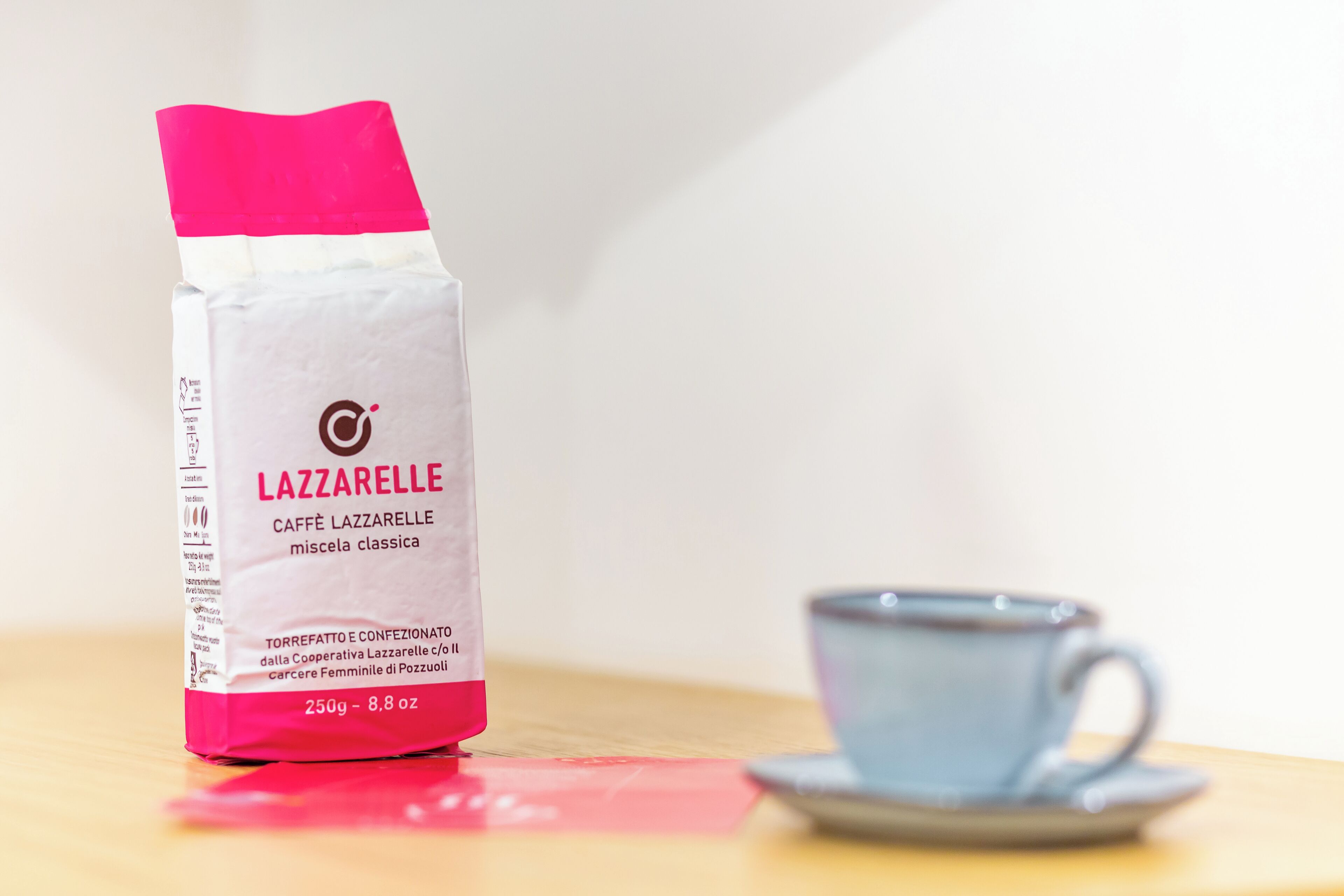 A bag of Lazzarelle coffee next to a cup on a table.