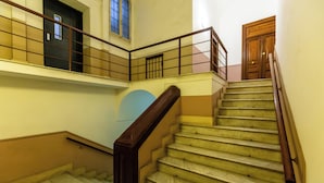 Una scala con corrimano in legno e gradini color beige, che conduce a un pianerottolo con una porta e una finestra.