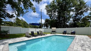 A rectangular swimming pool with a tiled deck, surrounded by a white fence, and shaded by trees. - Private Pool, Pet-Friendly, New 3BR Home in Cherry Grove (North Myrtle Beach)