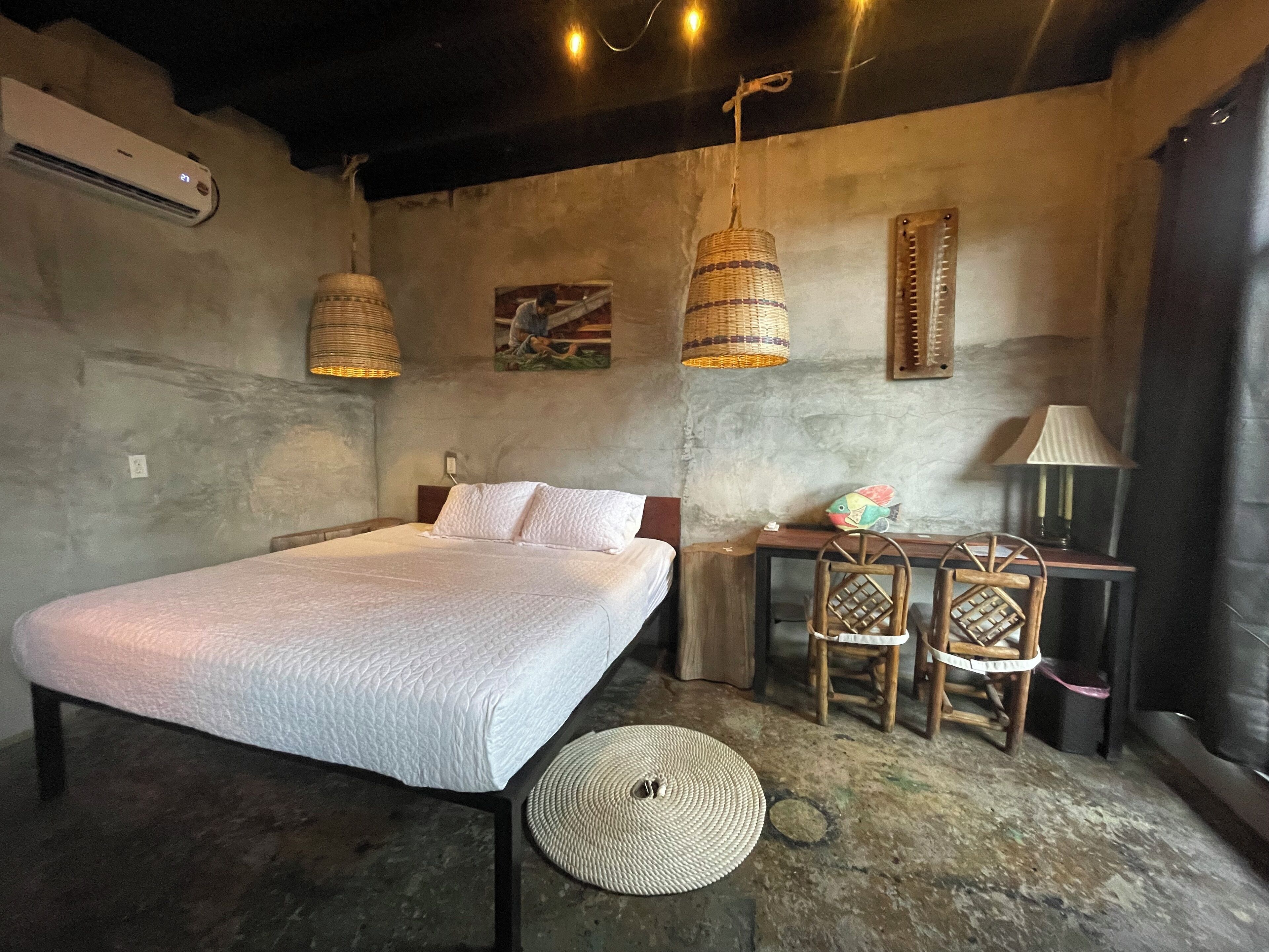 A bedroom with a bed, a desk, two chairs, a lamp, and a hanging light fixture.