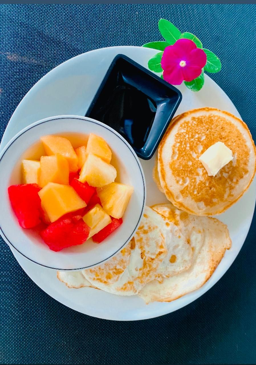 A plate with pancakes, fruit, and a small container of syrup.