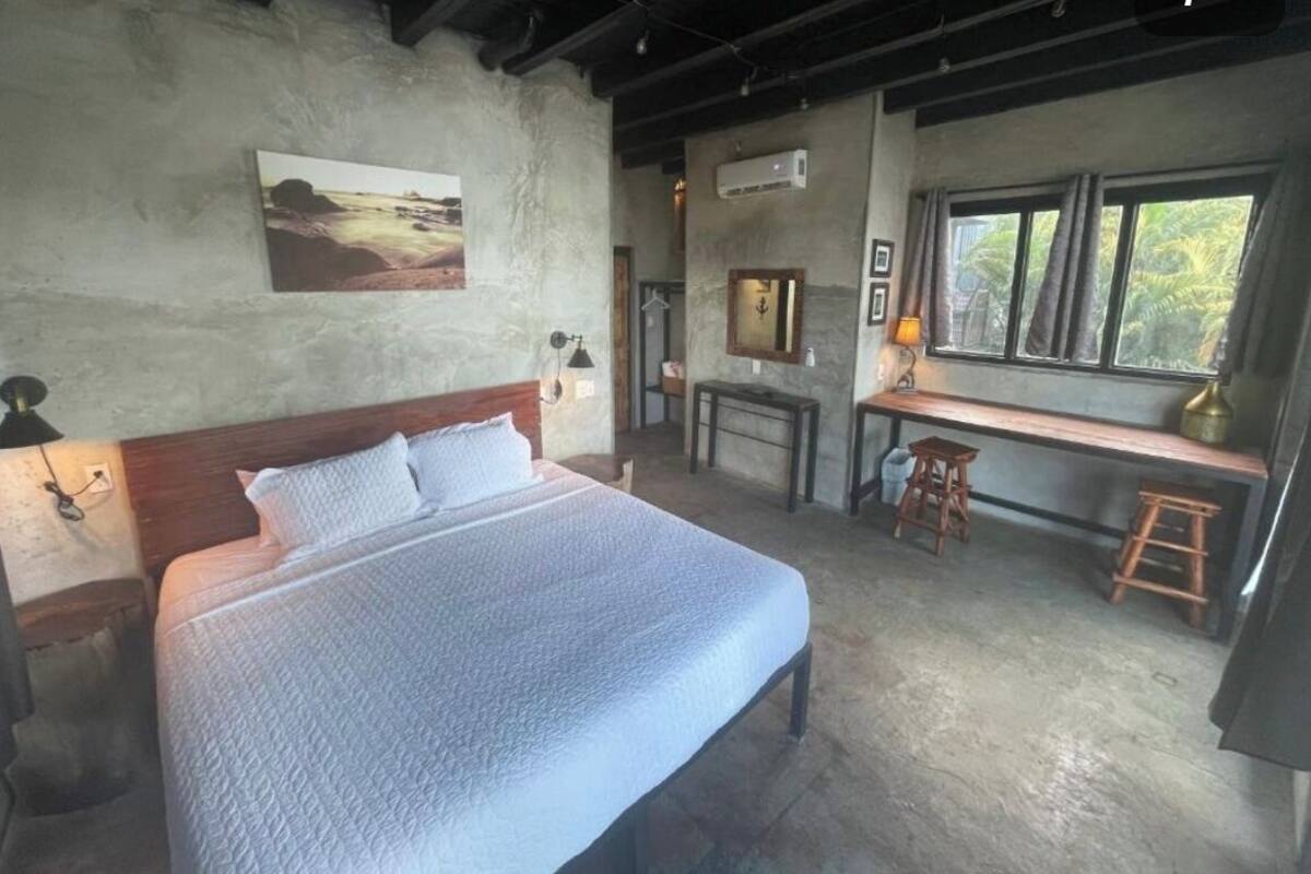 A bedroom with a large bed, a desk, and a window with a view of greenery.