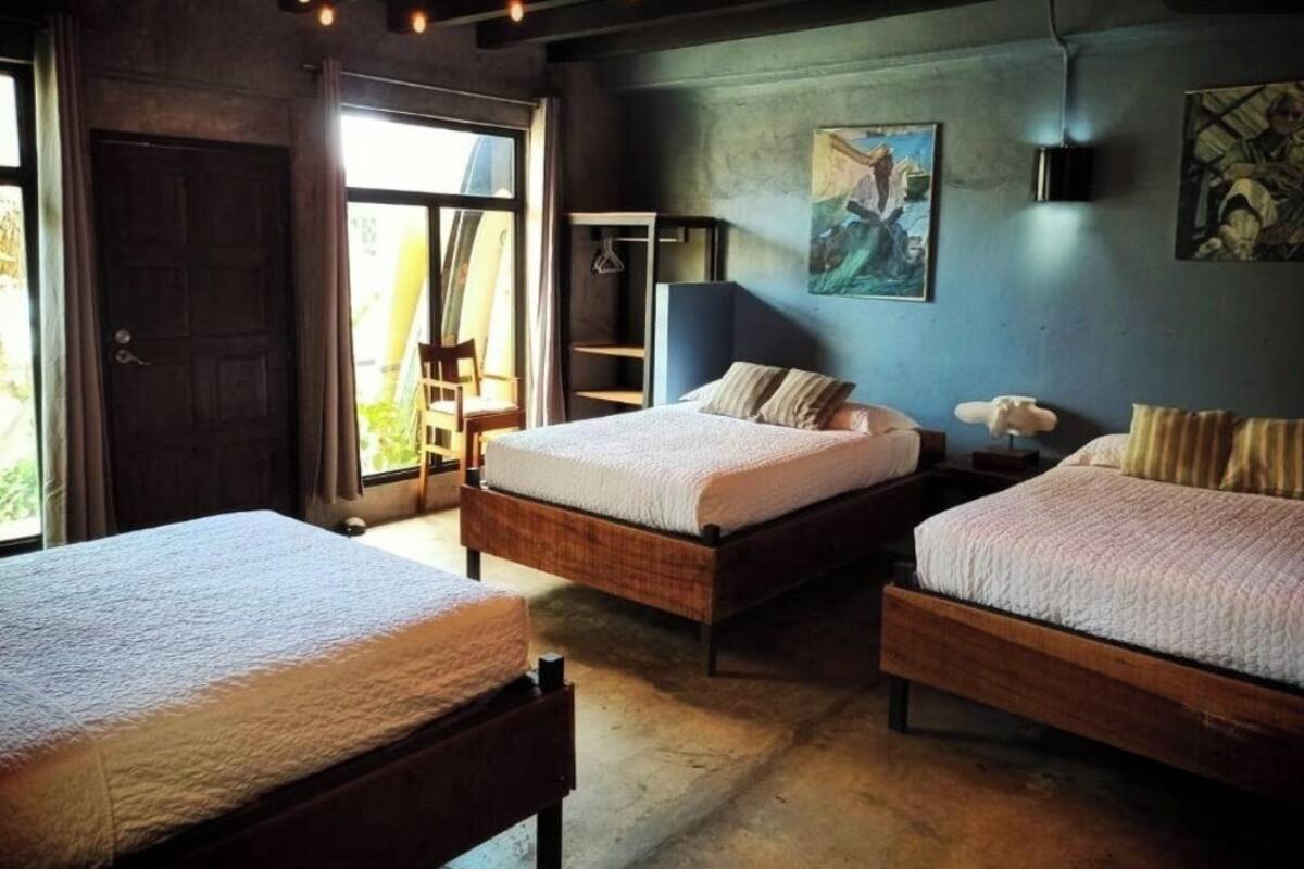 A bedroom with two wooden beds, a large window, and a painting on the wall.