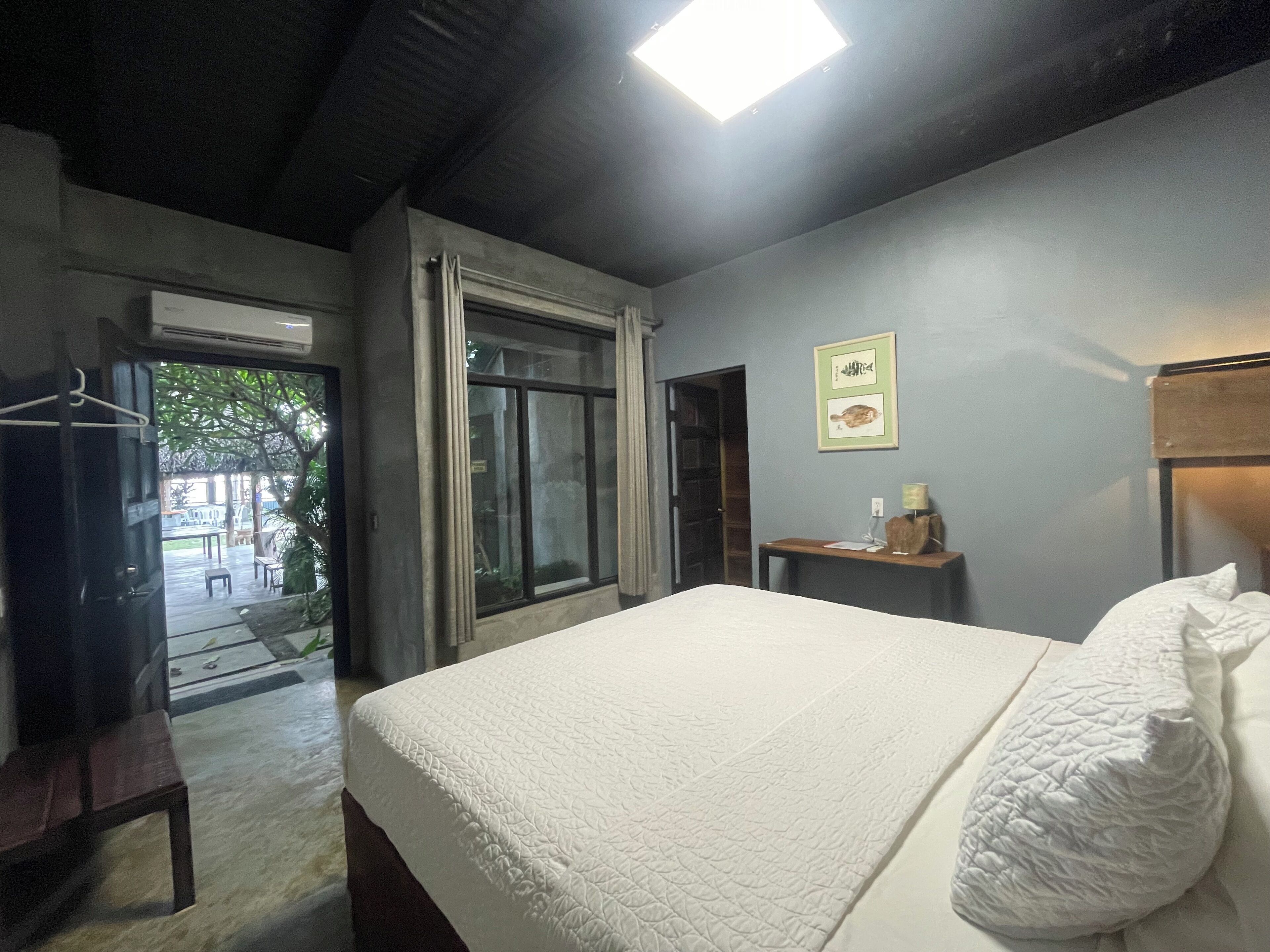 Quarto de hotel com cama, escrivaninha, cadeira e janela.