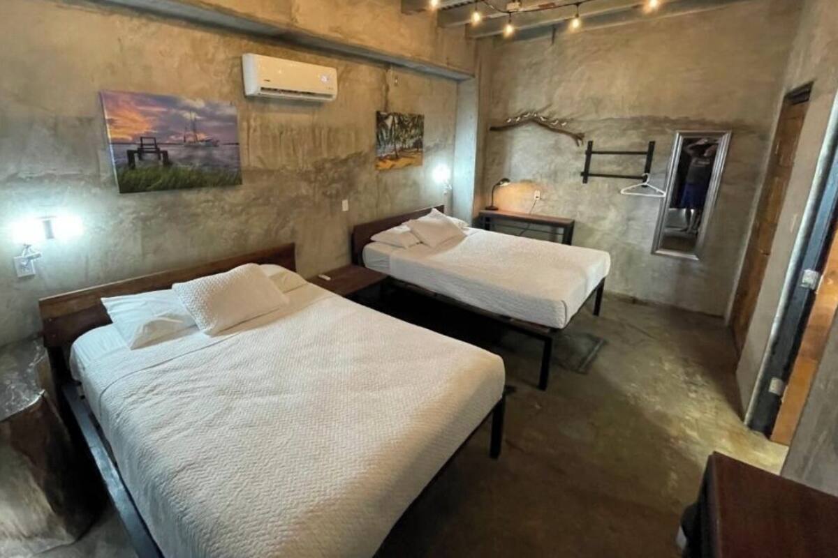 A room with two beds, a hanging light fixture, and a painting on the wall.