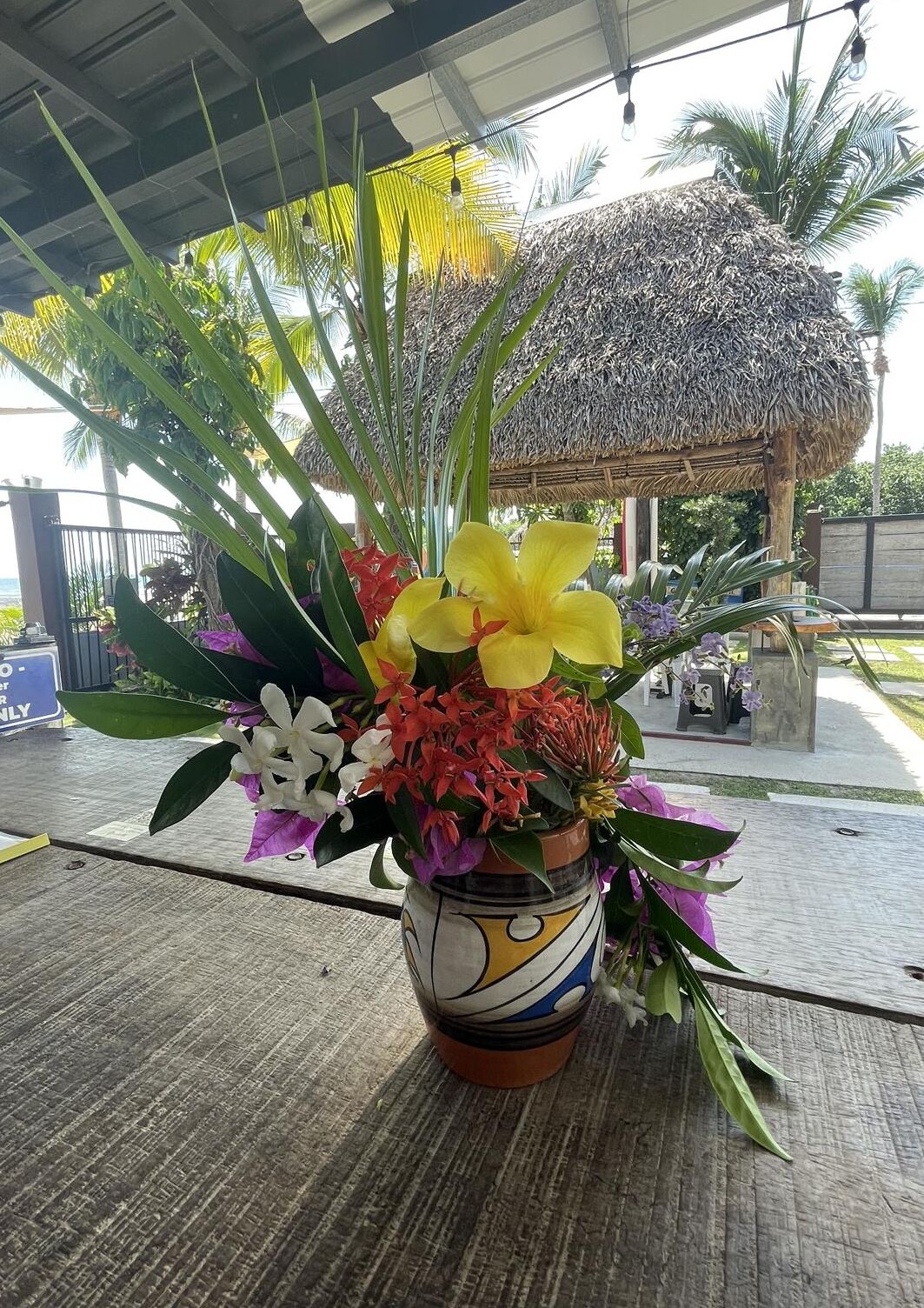 Un arrangement floral aux couleurs vives, présenté dans un pot décoratif sur une table en bois.