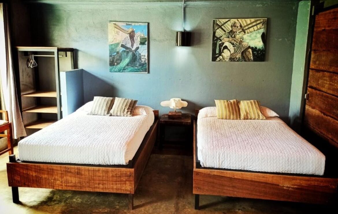 Una habitación con dos camas de madera, una mesita de noche pequeña y un estante fijado a la pared.