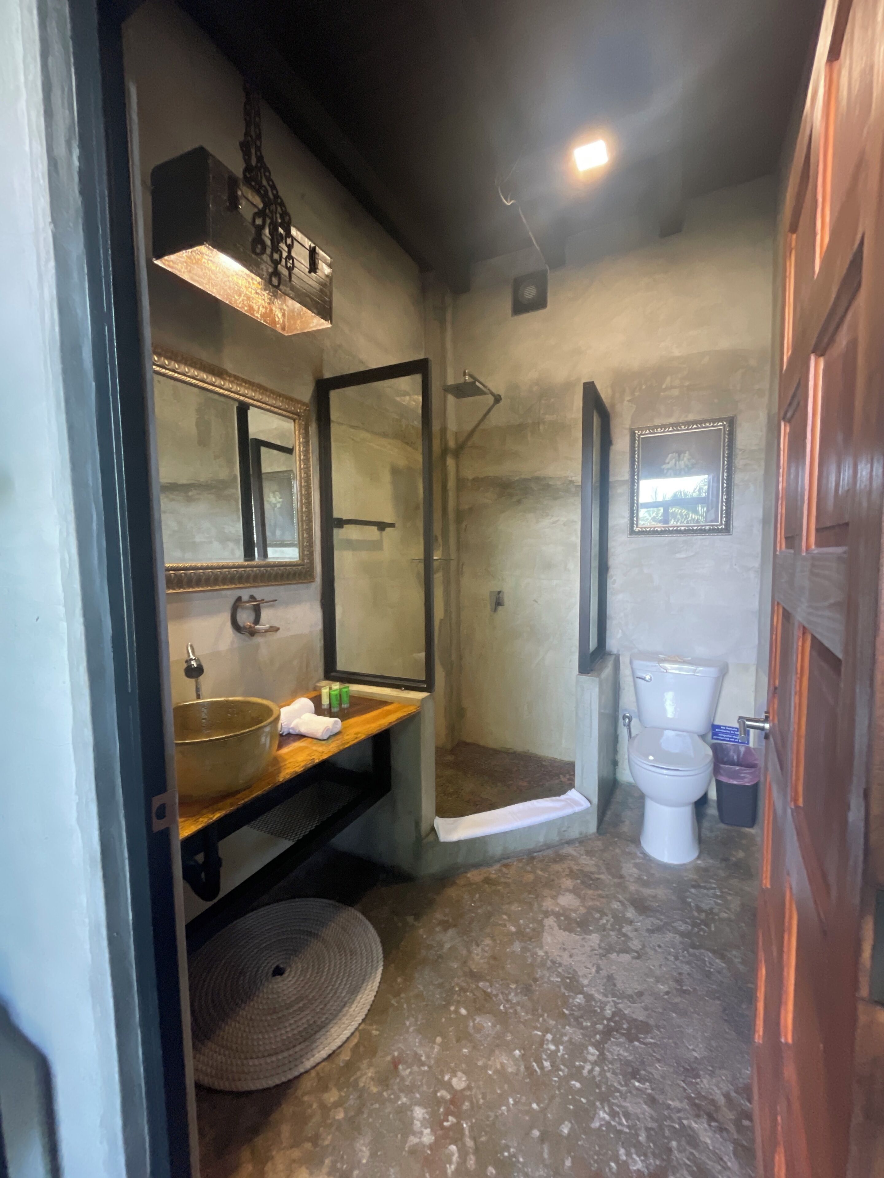 Un bagno con un grande specchio, un mobile bagno in legno, un lavandino in vetro, una doccia e un water.