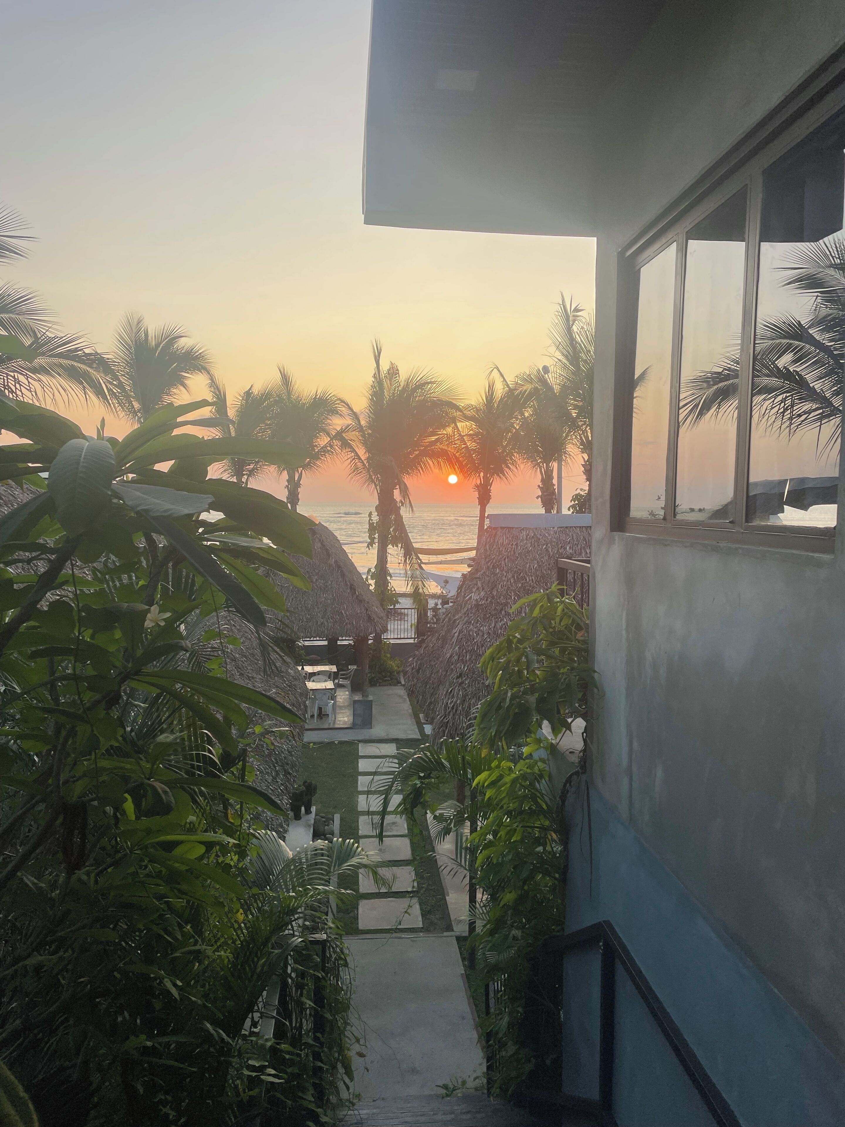 Una escalera que baja a una playa con palmeras y construcciones de techo de paja.