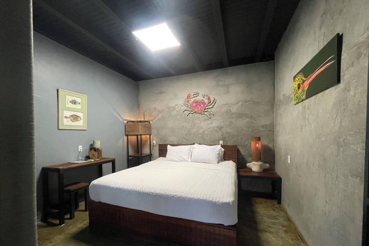 A bedroom with a bed, a desk, a chair, a lamp, and a wall-mounted artwork.