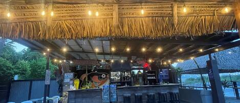An outdoor bar area with a thatched roof, string lights, and a reception desk.