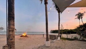 A beach scene with a fire pit, palm trees, and a view of the ocean.