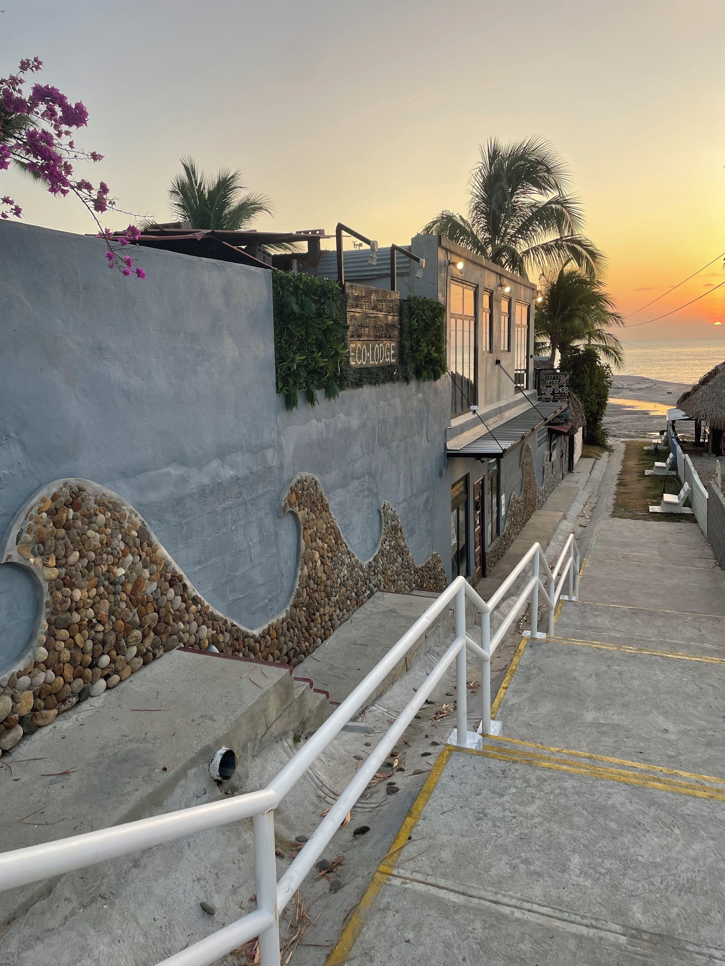 A coastal walkway with a concrete path, metal railings, and a stone wall with a wave design.