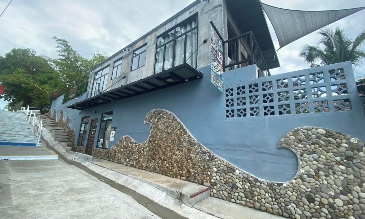 A building with a wave-like design on the facade, a staircase leading to the entrance, and a shaded area with a canopy.