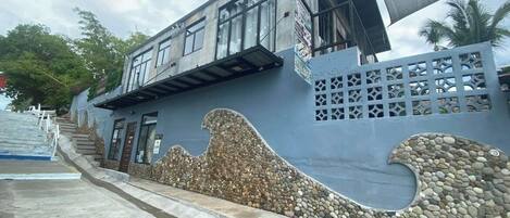 A building with a wave-like design on the facade, a staircase leading to the entrance, and a shaded area with a canopy.