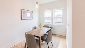 Een eetruimte met een houten tafel, vier stoelen, een vaas met een plant en een hanglamp.