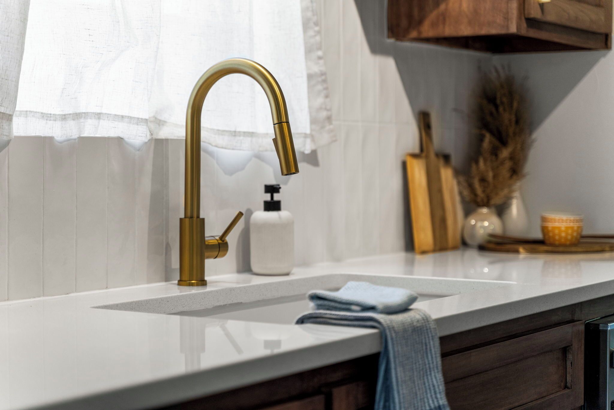 A modern kitchen with a white countertop, a gold faucet, and a white soap dispenser.