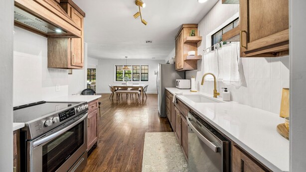 A modern kitchen with wooden cabinets, stainless steel appliances, and a white countertop.