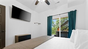 Un dormitorio con cama, televisor montado en la pared, cómoda de madera y ventana con cortinas.
