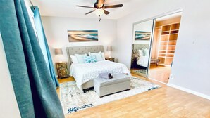 Un dormitorio con cama, mesitas de noche, ventilador de techo y vistas a otra habitación.
