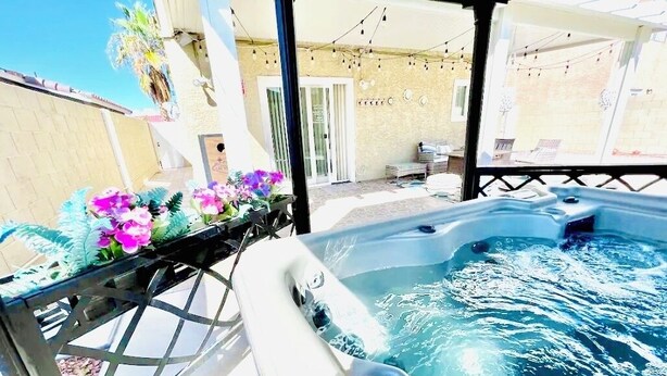 Un jacuzzi con estructura metálica y un patio con flores y una mesa.