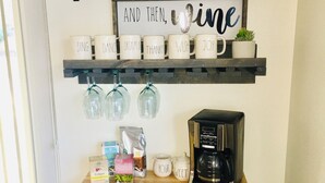 Una encimera de cocina con una cafetera, tazas y un letrero que dice 'PRIMERO, Café Y DESPUÉS, Vino'.