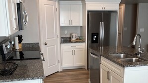A modern kitchen with white cabinets, granite countertops, a stainless steel refrigerator, and a built-in oven. - Cozy all season retreat, center of town! (Garden City)