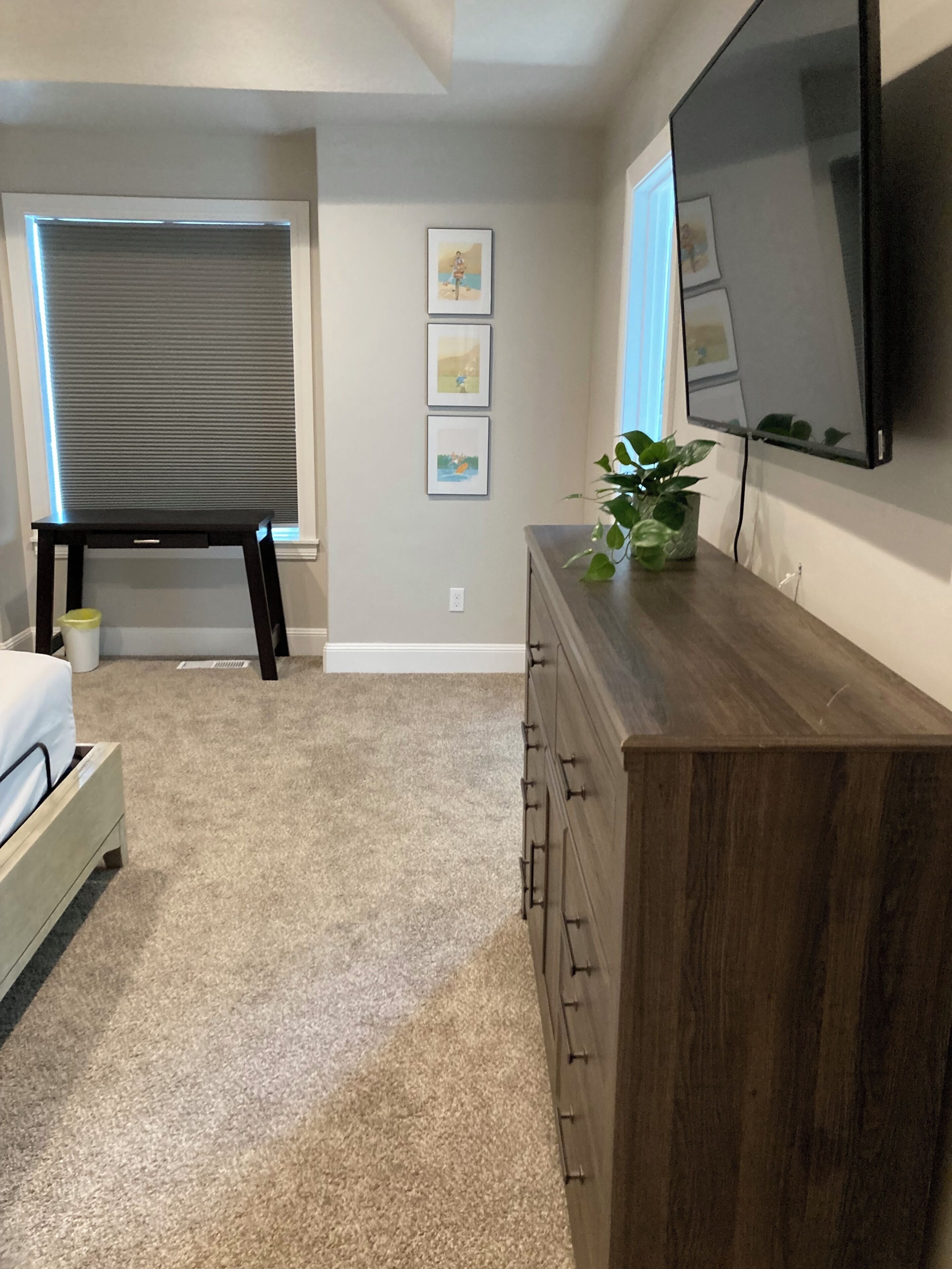 Un dormitorio con cama, cómoda, televisor y ventana con persianas.
