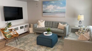 A living room with a sofa, ottoman, and a television. - Cozy all season retreat, center of town! (Garden City)