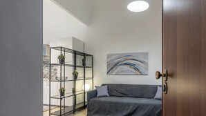 A modern living room with a grey sofa, a black metal shelving unit with plants, and a large abstract painting on the wall. - Al Khalisa Apartment by Wonderful Italy (Palermo)