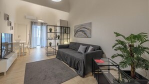 A modern living room with a grey sofa, a glass coffee table, a grey rug, a potted plant, and a painting on the wall. - Al Khalisa Apartment by Wonderful Italy (Palermo)