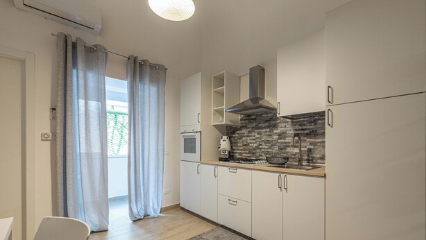 A modern kitchen with white cabinets, a built-in stove, and a stone backsplash. - Al Khalisa Apartment by Wonderful Italy (Palermo)