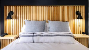 Un lit avec une tête de lit en bois, deux lampes de chevet et un coussin à rayures.